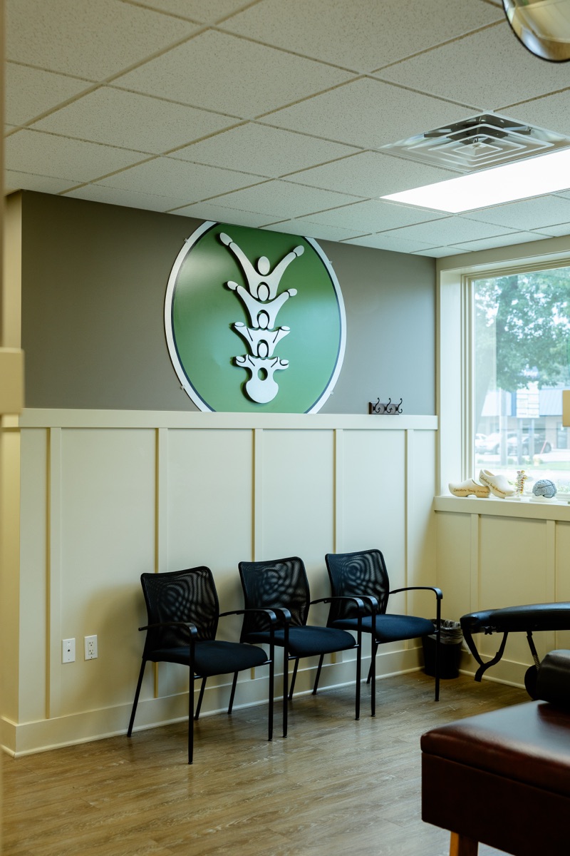 Waiting area at Lakeshore Family Chiropractic with the green practice emblem on the wall
